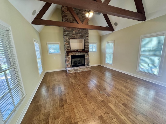 unfurnished living room featuring beam ceiling, high vaulted ceiling, a stone fireplace, and wood-type flooring