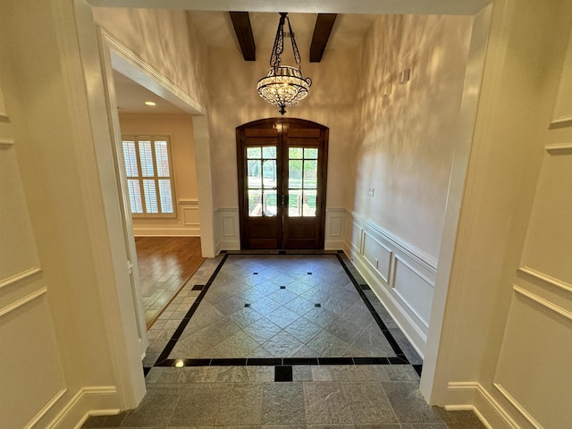 foyer entrance featuring a notable chandelier, beam ceiling, and french doors