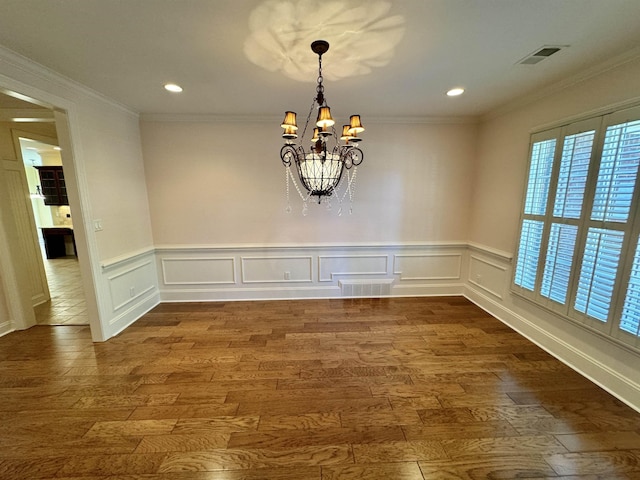 unfurnished dining area featuring hardwood / wood-style flooring, crown molding, and a chandelier