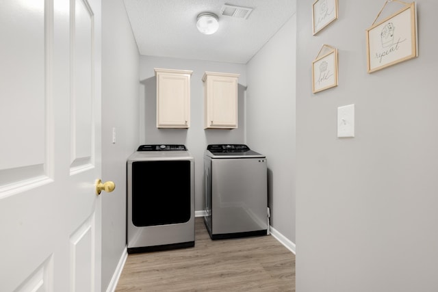 clothes washing area featuring cabinets, light wood-type flooring, a textured ceiling, and washing machine and dryer