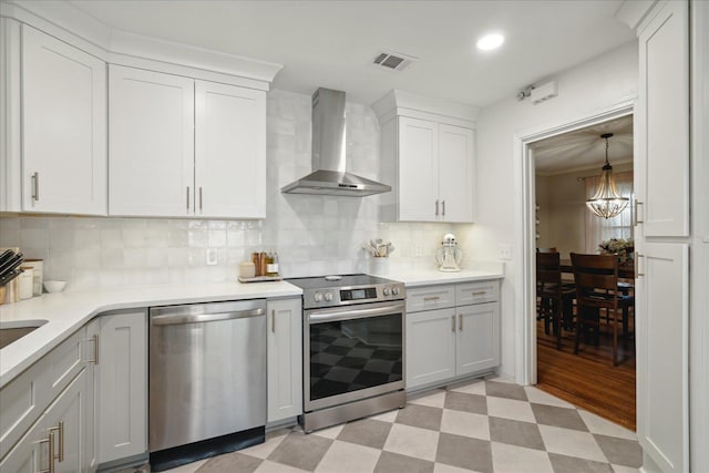 kitchen with backsplash, white cabinets, wall chimney range hood, a notable chandelier, and stainless steel appliances