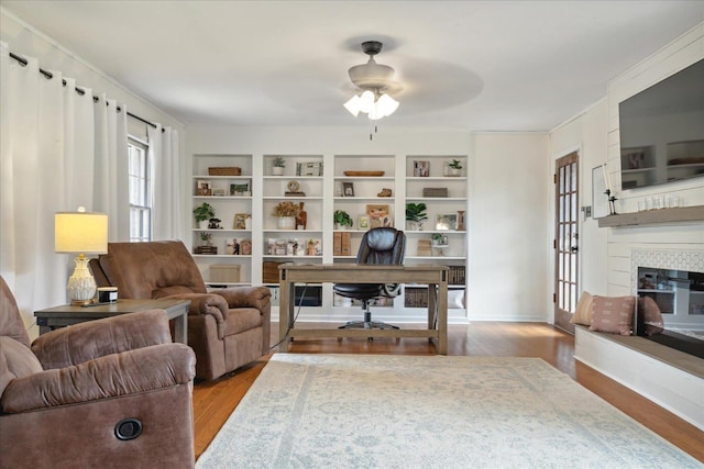 office area featuring a fireplace, ceiling fan, light hardwood / wood-style flooring, and built in shelves