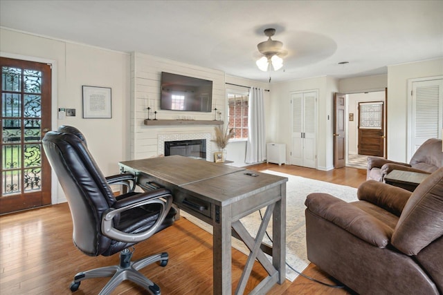 office with a fireplace, ceiling fan, radiator heating unit, and light hardwood / wood-style flooring