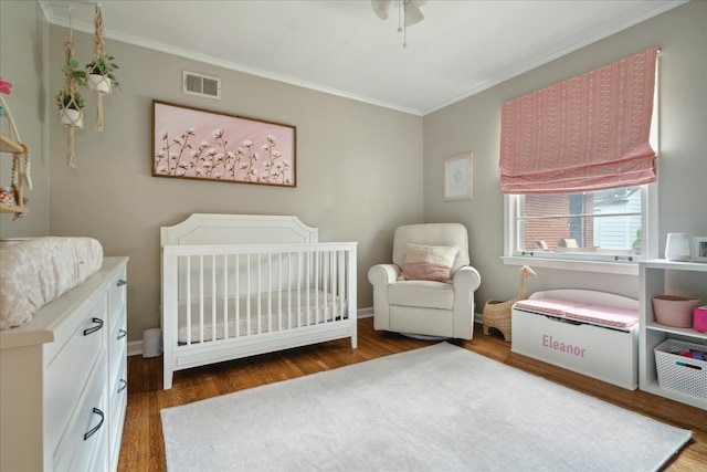 bedroom featuring dark hardwood / wood-style floors, a nursery area, crown molding, and ceiling fan