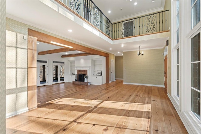 unfurnished living room featuring hardwood / wood-style floors, an inviting chandelier, ornamental molding, a towering ceiling, and a fireplace