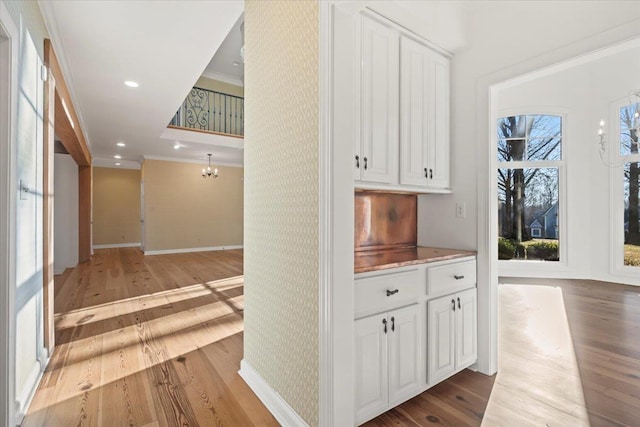 hallway with a notable chandelier, a healthy amount of sunlight, ornamental molding, and light hardwood / wood-style flooring