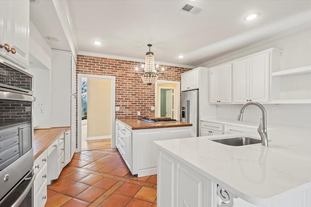 kitchen featuring sink, brick wall, pendant lighting, white cabinets, and appliances with stainless steel finishes