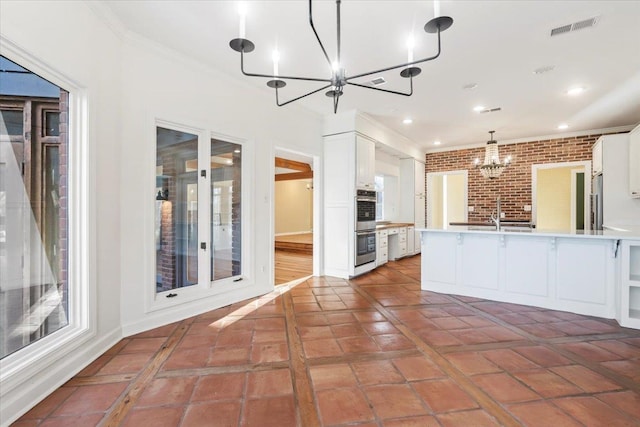 kitchen with white cabinetry, sink, stainless steel appliances, brick wall, and pendant lighting