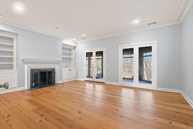 unfurnished living room featuring built in shelves, light wood-type flooring, french doors, and ornamental molding