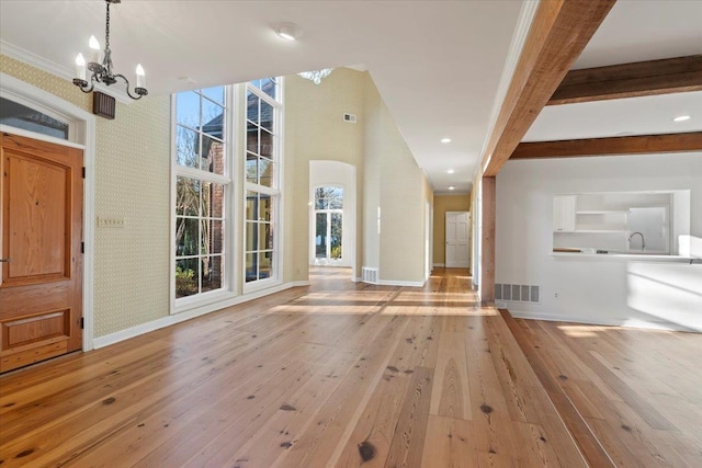 entryway with beamed ceiling, a notable chandelier, crown molding, and light hardwood / wood-style flooring