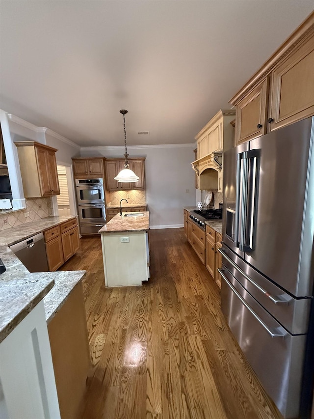 kitchen with a kitchen island with sink, sink, hanging light fixtures, decorative backsplash, and appliances with stainless steel finishes