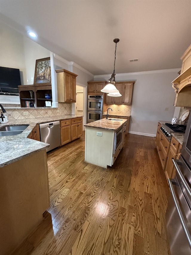 kitchen featuring a kitchen island with sink, sink, hanging light fixtures, light stone countertops, and appliances with stainless steel finishes