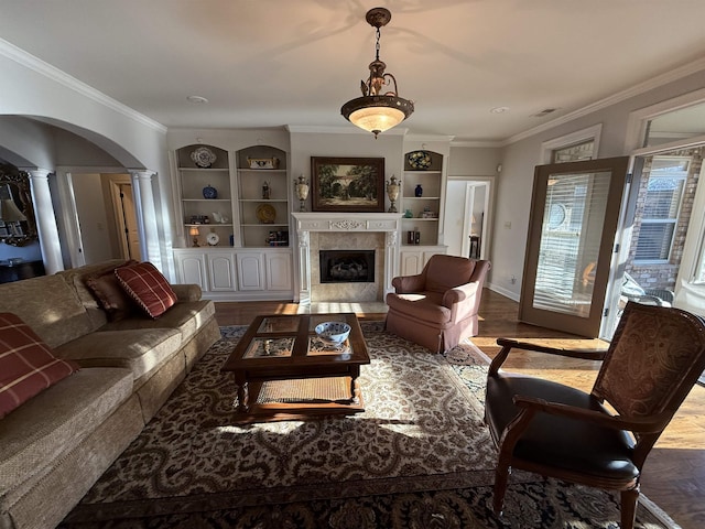 living room with a high end fireplace, crown molding, hardwood / wood-style flooring, built in shelves, and ornate columns