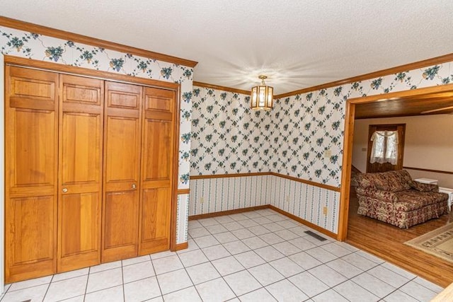 interior space featuring light tile patterned flooring, pendant lighting, a textured ceiling, and ornamental molding