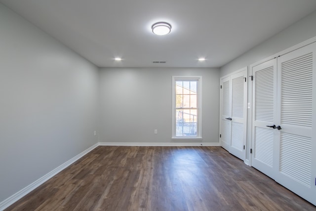 unfurnished bedroom featuring two closets and dark wood-type flooring