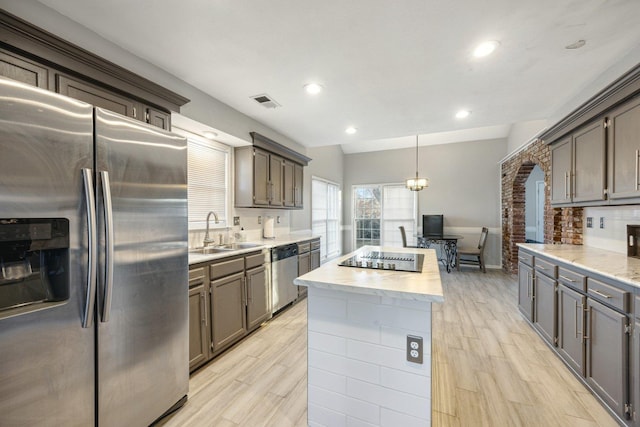 kitchen with stainless steel appliances, sink, decorative light fixtures, light hardwood / wood-style floors, and a kitchen island