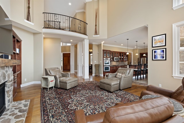 living room featuring hardwood / wood-style floors, a towering ceiling, decorative columns, and a stone fireplace