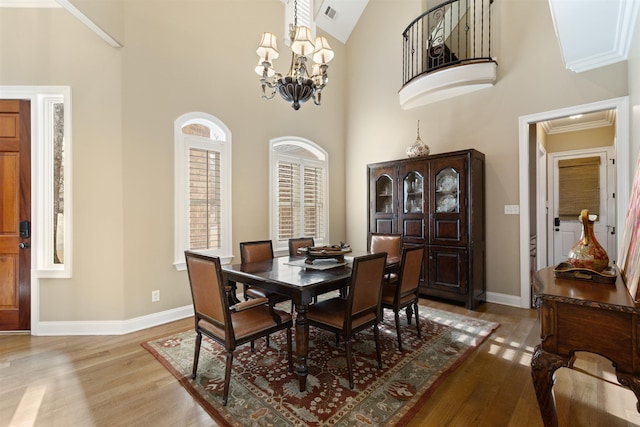 dining room featuring a high ceiling, light wood-type flooring, crown molding, and a notable chandelier