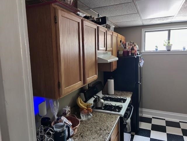 kitchen with a paneled ceiling, light stone counters, and white gas range