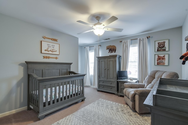 carpeted bedroom with ceiling fan and a crib