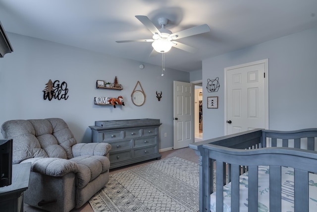 carpeted bedroom featuring ceiling fan and a nursery area