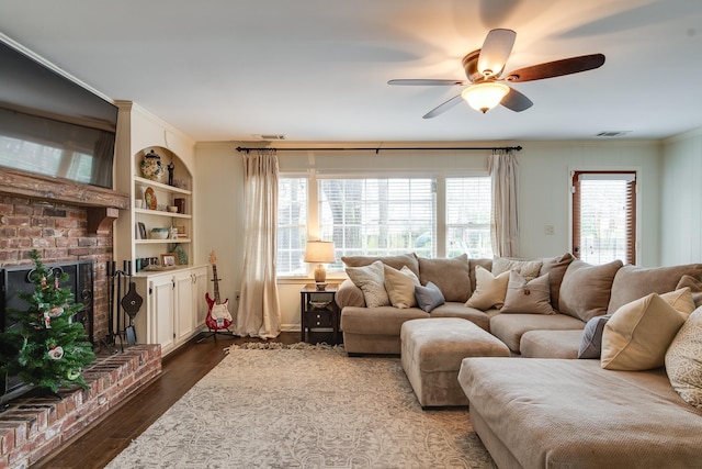 living room with dark wood-type flooring, built in shelves, ceiling fan, a fireplace, and a healthy amount of sunlight