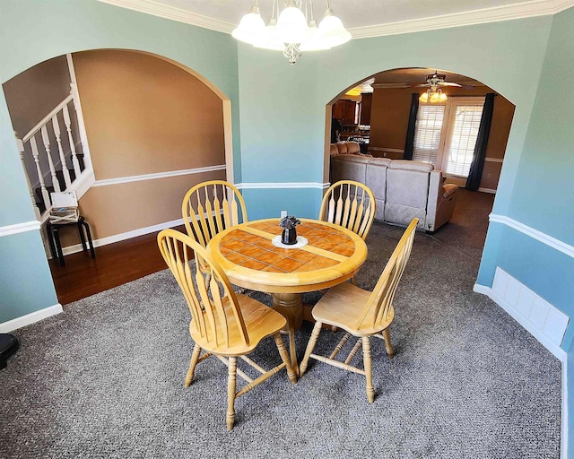 dining space with ornamental molding, ceiling fan with notable chandelier, and dark colored carpet