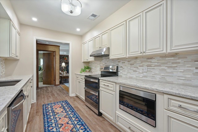 kitchen featuring white cabinets, light hardwood / wood-style flooring, decorative backsplash, light stone countertops, and stainless steel appliances