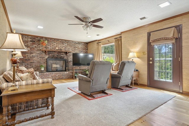 living room featuring crown molding, a brick fireplace, ceiling fan, a textured ceiling, and light hardwood / wood-style floors