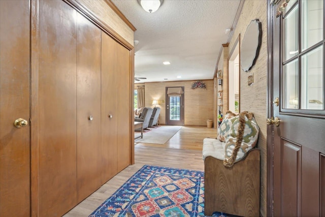 corridor with a textured ceiling, light wood-type flooring, and crown molding