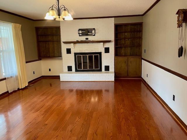 unfurnished living room featuring a chandelier, a brick fireplace, hardwood / wood-style flooring, and built in features