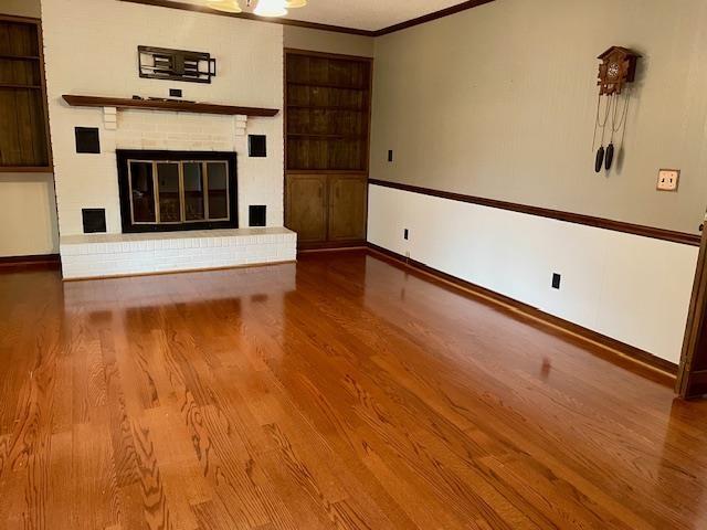 unfurnished living room with built in shelves, crown molding, a fireplace, and hardwood / wood-style flooring