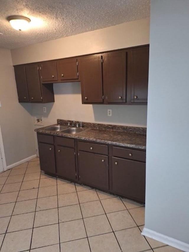 kitchen featuring a textured ceiling, sink, light tile patterned floors, and dark brown cabinets