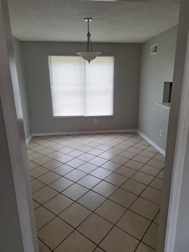 unfurnished dining area featuring a textured ceiling and light tile patterned flooring