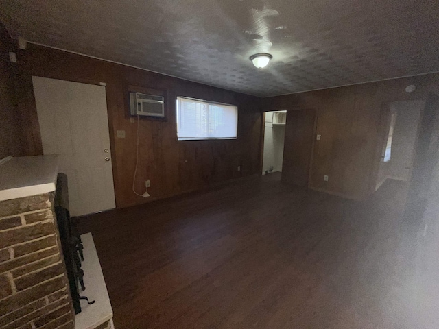 unfurnished living room featuring an AC wall unit, wooden walls, a textured ceiling, and dark hardwood / wood-style floors