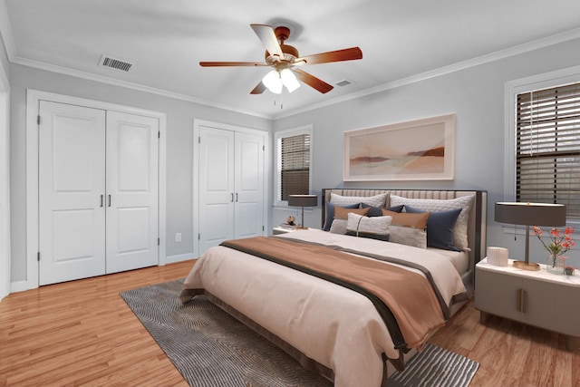 bedroom featuring ceiling fan, light wood-type flooring, crown molding, and multiple closets