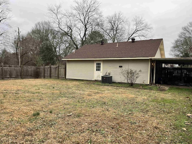 rear view of property with fence, a yard, roof with shingles, an attached carport, and central AC unit