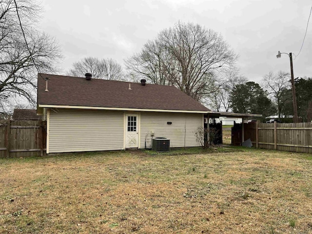 rear view of property with cooling unit, fence, a lawn, and roof with shingles