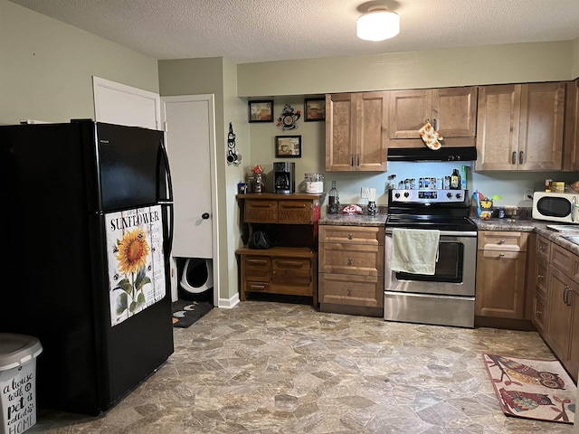 kitchen with under cabinet range hood, stainless steel electric range oven, dark countertops, and freestanding refrigerator