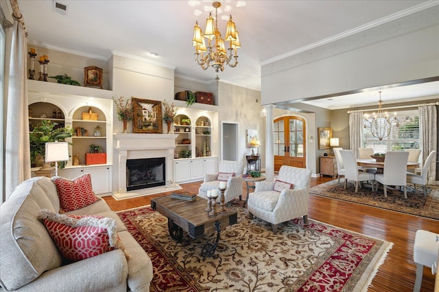 living room with built in shelves, light hardwood / wood-style floors, ornamental molding, and an inviting chandelier