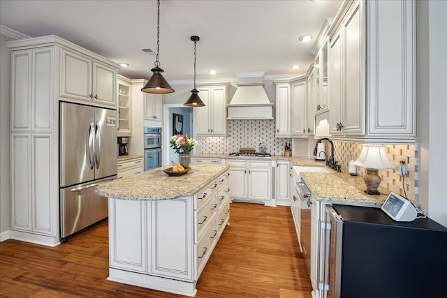 kitchen featuring sink, premium range hood, decorative light fixtures, a kitchen island, and appliances with stainless steel finishes