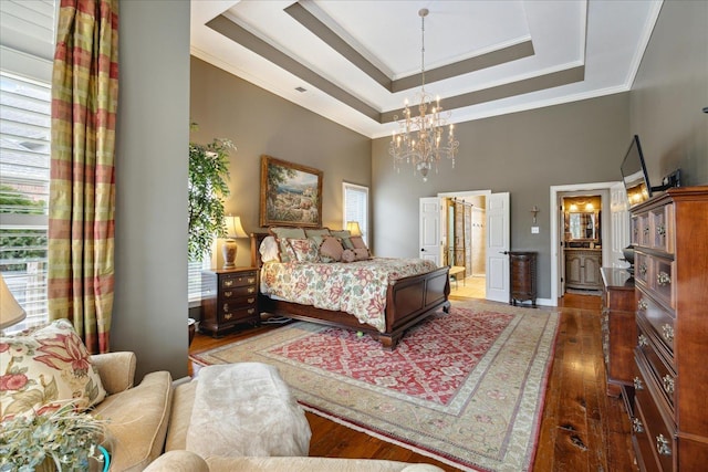 bedroom featuring connected bathroom, a raised ceiling, crown molding, a chandelier, and hardwood / wood-style flooring