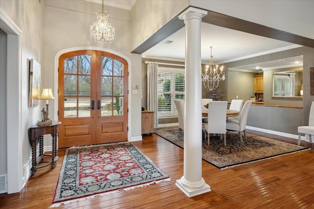 foyer entrance featuring hardwood / wood-style flooring, a notable chandelier, ornate columns, and french doors