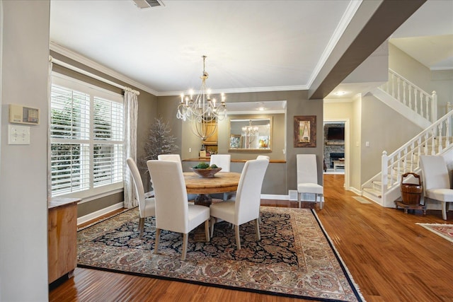 dining area with a notable chandelier, a stone fireplace, wood-type flooring, and crown molding