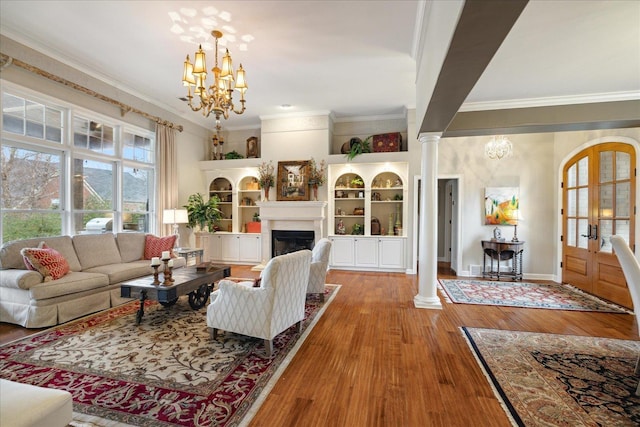 living room with hardwood / wood-style floors, ornate columns, ornamental molding, and an inviting chandelier