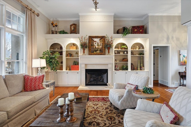 living room with hardwood / wood-style flooring, built in shelves, and ornamental molding