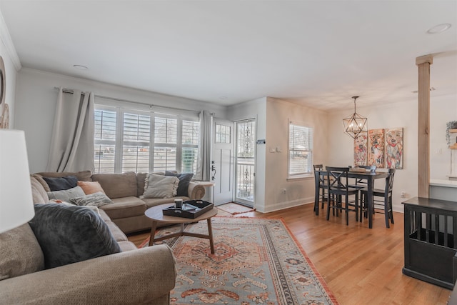 living room featuring ornate columns, a notable chandelier, ornamental molding, and light hardwood / wood-style flooring