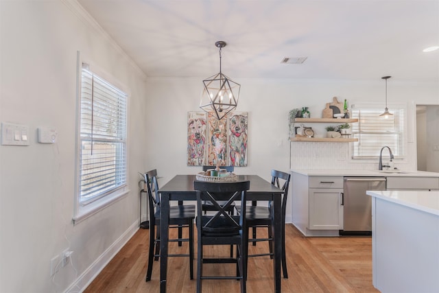 dining area featuring light hardwood / wood-style floors, sink, ornamental molding, and a chandelier