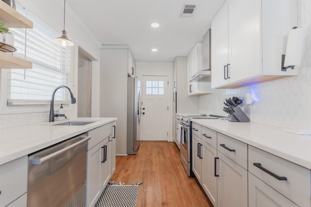 kitchen featuring sink, white cabinetry, light hardwood / wood-style flooring, stainless steel appliances, and wall chimney exhaust hood