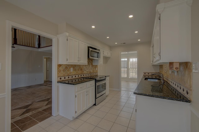 kitchen with dark stone counters, stainless steel appliances, sink, light tile patterned floors, and white cabinets